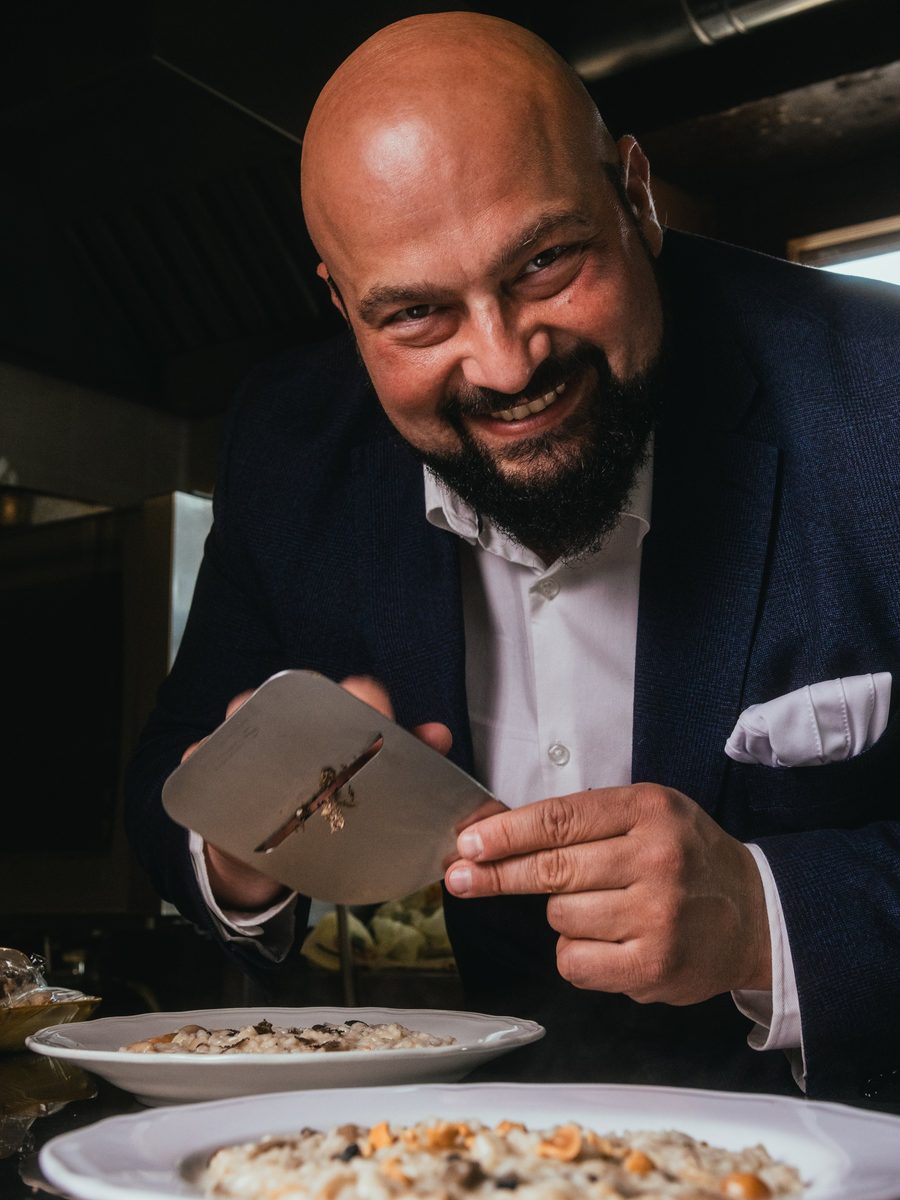 Daniele Violoni in cucina, con l'affetta-tartufo sopra due piatti di risotto