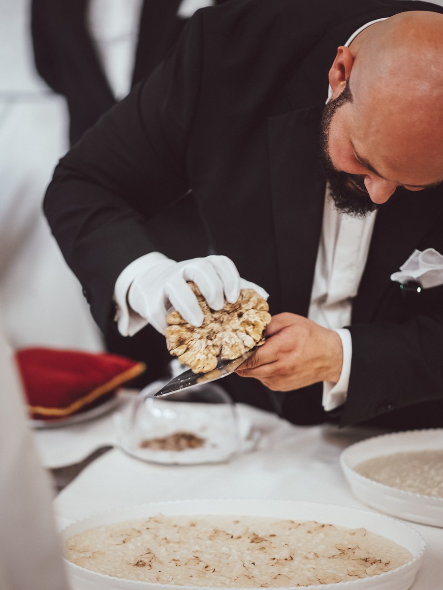Daniele Violoni affetta il Tartufo Bianco con i guanti bianchi sopra il piatto, al tavolo